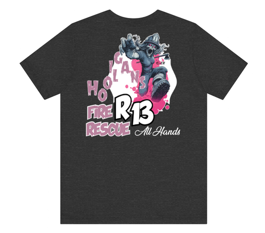 A dark heather gray t-shirt featuring a large graphic print on the front. The graphic depicts a firefighter in a dynamic pose with the text 'HOLICAN FIRE RESCUE', 'R13', and 'All Hands' in pink, white, and black.